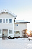 White, two-storey wooden house in snow-covered garden