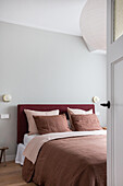 Bed in soft red tones in simple bedroom
