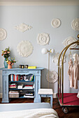 Light blue bookcase, suitcase trolley and plaster rosettes on wall of bedroom