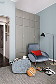 Grey wardrobe, armchair and pouffe in teenager's bedroom with blue walls