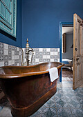 Freestanding bathtub in guest bathroom with blue wall and wall tiles