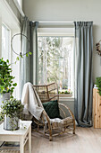 Rustic rattan armchair in front of window with floor length curtains