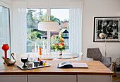 Tray and book on kitchen counter in front of oval dining table with candles next to window