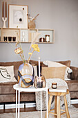 Glasvase mit Trockenblumen, Kerze und Windlicht auf Beistelltisch vor Sofa mit Kissen