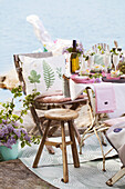 Kissen mit botanischem Druck auf Stuhl, Hocker und festlich gedeckter Tisch am See