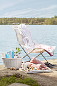 Deck chair next to basket and tray of spa and bathing utensils by a lake