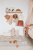 Krabbeldecke, darüber Garderobe mit Mädchenkleidung im Kinderzimmer in Nude-Tönen