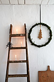 Leiterregal mit Kerzen und Weihnachtskranz vor weißer Wand