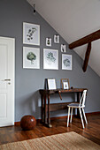 Rustikaler Arbeitstisch mit Stuhl an grauer Wand mit botanischen Zeichnungen