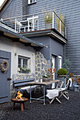 Terrasse mit Feuerstelle und Sitzgelegenheiten vor einem Haus in Grautönen