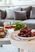 Red grapes on a plate and two glasses of wine on coffee table