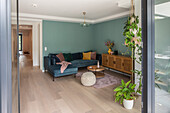 Corner sofa, low sideboard, coffee table and potted plants in living room with green walls