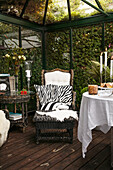 Round table set with tablecloth, armchair with animal-print cushion and footstool in conservatory