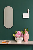 Vase of flowers on console table below mirror and wall lamp on green wall