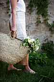 Frau trägt Korbtasche mit weißem Strauß aus Pfingstrosen, Schneeball, Mutterkraut und Gräsern