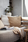 Gemütliches Sofa mit Kissen, Decke und Buch, dahinter Trockenstrauß aus Kugeldisteln