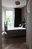 Blick auf Doppelbett im Schlafzimmer mit Backsteinwand und Fenstertür