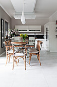 Dining table and chairs below pendant lights in front of kitchen in open-plan interior