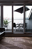 Leather couch in living room with herringbone parquet floor: view of table, chairs and parasol on balcony