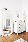 White chest of drawers and mirror on wooden floorboards