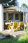 Terrasse mit Tisch und gelben Stühlen vor Gartenhaus