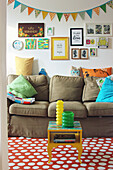 Sofa with scatter cushions below pictures and bunting on the wall and small table on polka-dot rug