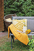 Garnrollen, Schafgarbe, gelbe Decke und Kissen auf Gartenbank