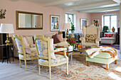 Verschiedene Sitzmöbel im Wohnzimer mit blassrosa Wänden und weißer Holzbalkendecke