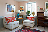 Two armchairs with decorative cushions, side table and piano in the room with pale pink walls