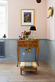 Antique end table, footstool in front of it in the room with pale pink walls