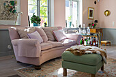Green upholstered ottoman and a pink sofa with cushions, next to it bar cart in the living room