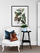 White armchair with cushion and bag next to stele with indoor plant