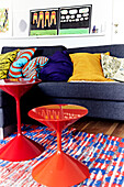 Colourful retro-style living room with red side tables, sofa with lots of cushions and murals
