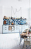 Light kitchenette, graphic tiled wall above, dining area in the foreground