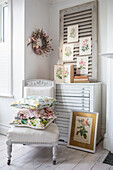 Pale interior with antique chair, floral cushions and vintage french shutter