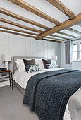 Double bed in guest bedroom with white panelled wall and wood-beamed ceiling