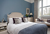 Double bed with headboard and sofa in cream shades in guest bedroom with blue walls