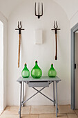 Console table with green balloon bottles and old garden tools on the wall