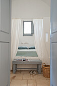 View into simple bedroom of double bed with canopy and clothes bench