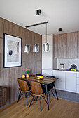 Small dining area next to wood-panelled wall and kitchen in open-plan interior