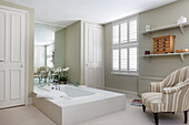 Elegant, spacious bathroom with sunken bathtub and striped armchair