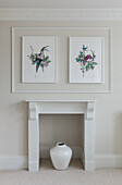 Vase in disused fireplace below pictures on wall