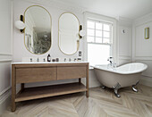 Free-standing bathtub by the window, double washbasin, mirror above in the bathroom