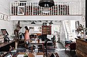 Open, rustic living room with whitewashed walls, gallery with stacks of books
