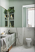Washstand and toilet in bathroom with marble-effect tiles and green walls