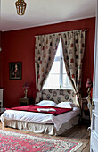 Double bed in front of curtained window in room with red walls