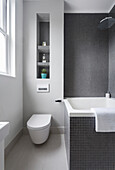 Badezimmer mit Badewanne, Toilette, Regale in Wandnische und Mosaikfliesen