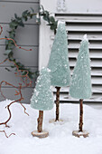 Three decorative, snow-covered miniature fir trees made of felt on wooden trunks