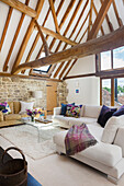 Seating and glass coffee table in a converted barn with natural stone wall and wooden beams