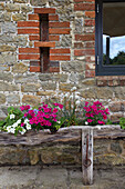 Flowerbed of rustic wooden trough in front of wall of natural stones and bricks